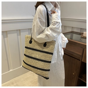Detail of hand-woven straw tote with black stripes and slender faux leather shoulder strap