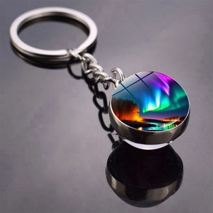 Double-sided aurora glass ball keychain with silver metal ring on black reflective surface