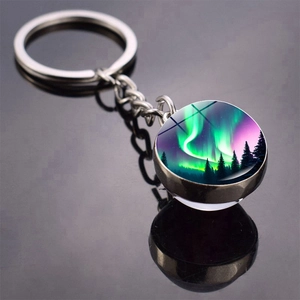 Close-up of double-sided glass ball keychain featuring aurora borealis and forest silhouette