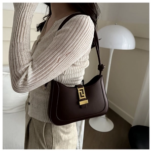 Detail of deep brown crescent shoulder bag with golden geometric hardware on a model