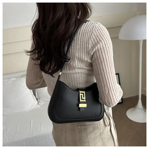 Detail of a black leather underarm bag with a gold geometric clasp on a model