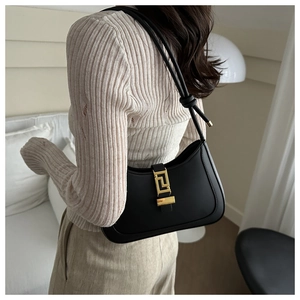 Detail of black hobo bag with gold geometric buckle worn by model in a modern room