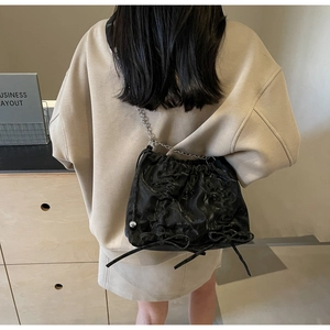 Detailed view of a black pleated bucket bag with metal chain strap and bow decorations