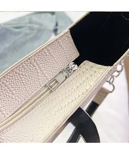 Detailed close-up of cream textured leather handbag with silver zipper and chain strap