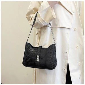 Detailed shot of black crocodile pattern shoulder bag with silver chain on beige trench coat