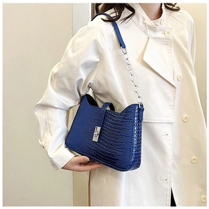 Detail of navy blue croc-embossed shoulder bag with silver twist lock on beige trench coat