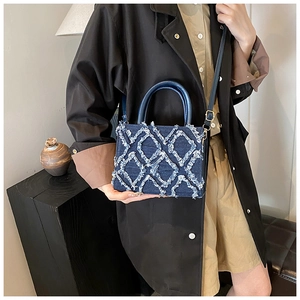 Detailed shot of dark blue denim bag with white fringe quilted pattern and round handles