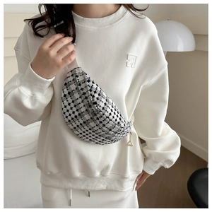 Detail of checkered crossbody bag with silver zipper and woven strap on white sweatshirt
