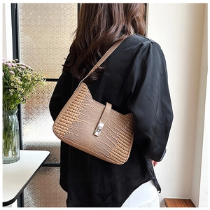 Detail of caramel brown crocodile texture shoulder bag with metallic lock shown on model