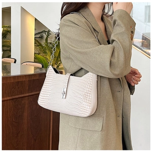 Detailed view of beige crocodile embossed underarm bag with silver chain on model