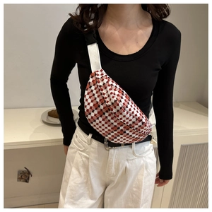 Close-up of stylish plaid waist bag with red and white woven pattern on a female model
