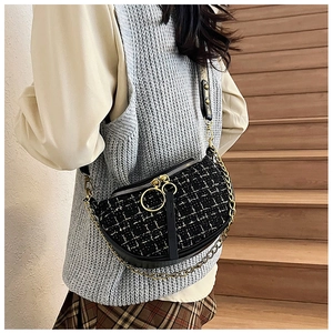 Detail view of a black and white tweed crossbody bag with gold chain and ring zippers