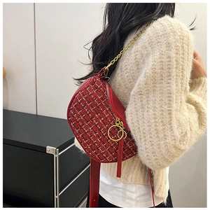 Detailed view of a red tweed saddle bag with gold chain strap on a beige sweater