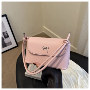 Gros plan du sac bandoulière rose avec fermoir papillon argenté dans un décor doux