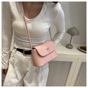 Détail du sac bandoulière rose clair avec nœud argenté porté sur un pull blanc