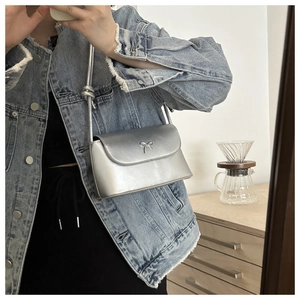 Close-up of a silver crossbody bag with a metallic finish and a butterfly bow detail