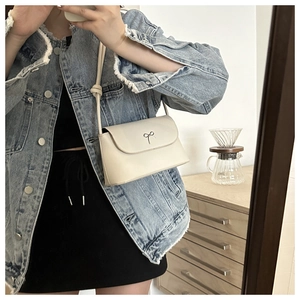 Close-up of cream crossbody bag featuring a silver butterfly buckle on a curved flap