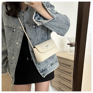 Gros plan sur le sac bandoulière beige avec boucle nœud en métal argenté sur rabat