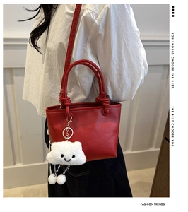 Detail of red litchi leather bucket bag featuring a white plush cloud charm and knotted handle
