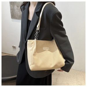 Detail of beige knit tote bag with silver chain strap worn by a model in a minimalist setting