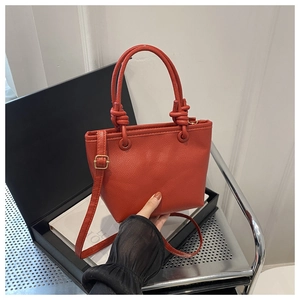 Detail of red lychee grain leather bucket bag featuring knot handle and golden hardware