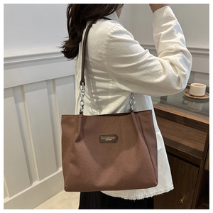Detail of a brown woven tote bag featuring a leather logo patch and metal chain strap