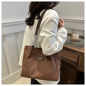 Detail of coffee brown tote bag showing textured fabric, leather strap, and chain handle