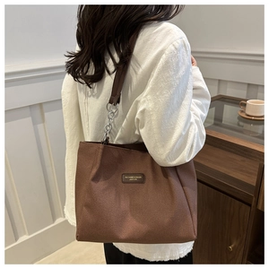 Detail of brown canvas tote bag with leather label and silver chain strap on model