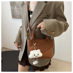 Detail showing brown lychee textured leather bucket bag with a cute white plush cloud charm