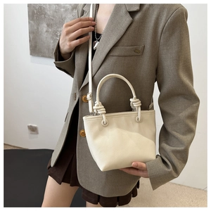 Detail of cream white leather bucket bag with litchi texture and elegant knot handle