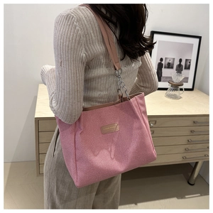 Detail of pink corduroy tote bag featuring leather logo patch and metal chain strap