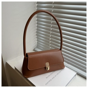 Detail of caramel brown leather handbag with gold metal clasp on white books background