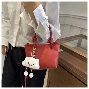 Dettaglio borsa tote rossa con texture litchi, manico a nodo e charm a nuvola bianca