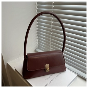 Close-up of a burgundy baguette shoulder bag with golden lock on a white book