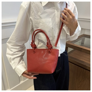 Detailed view of red pebble texture leather bucket bag featuring a unique knotted handle design