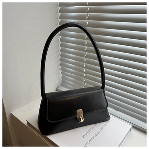 Detail of minimalist black leather underarm bag featuring a golden metal turn-lock closure