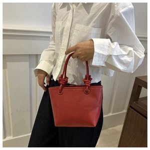 Close-up of red lychee textured leather bucket bag with knot handle detail for women