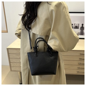 Close-up of black lychee-textured bucket bag with knot handle and shoulder strap