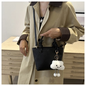 Close-up of black lychee leather bucket bag with white cloud plush charm detail