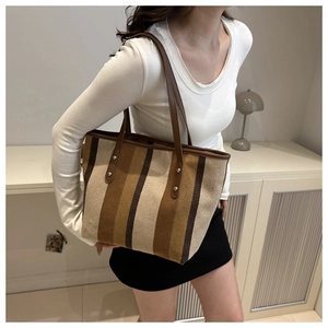 Detail of striped tote bag featuring brown leather straps and gold metal rivet accents