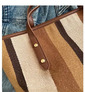 Close-up of striped fabric tote bag featuring brown leather handles and gold rivet details