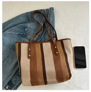 Detailed view of striped canvas tote bag with leather handles and size comparison to a phone