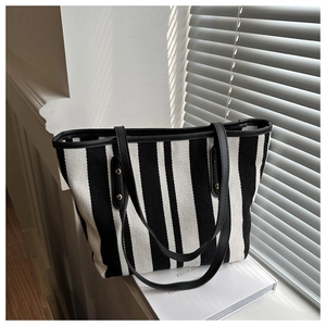 Detail of vertical striped canvas tote bag with black leather trim and metal rivets