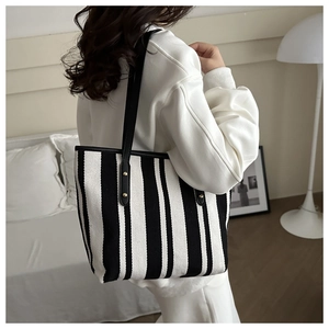 Lifestyle view of a black and white striped tote bag with gold rivets and black handles