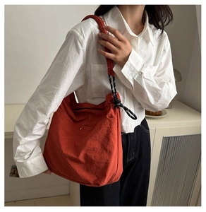 Detail view of large orange-red tote bag with thick woven rope strap on female model