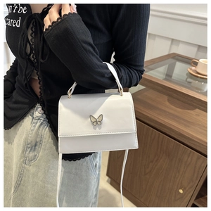 Detail of white square handbag featuring a butterfly metal buckle and slim leather strap
