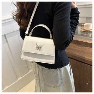 Detail view of a white PU leather crossbody bag with a metal butterfly buckle on a model