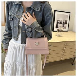 Detailed view of pink crossbody bag featuring decorative butterfly metal hardware