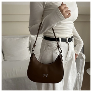 Detail of dark brown crescent underarm bag with silver bow accent on model's shoulder