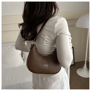 Detail of a brown leather crescent shoulder bag with a silver bow and adjustable strap